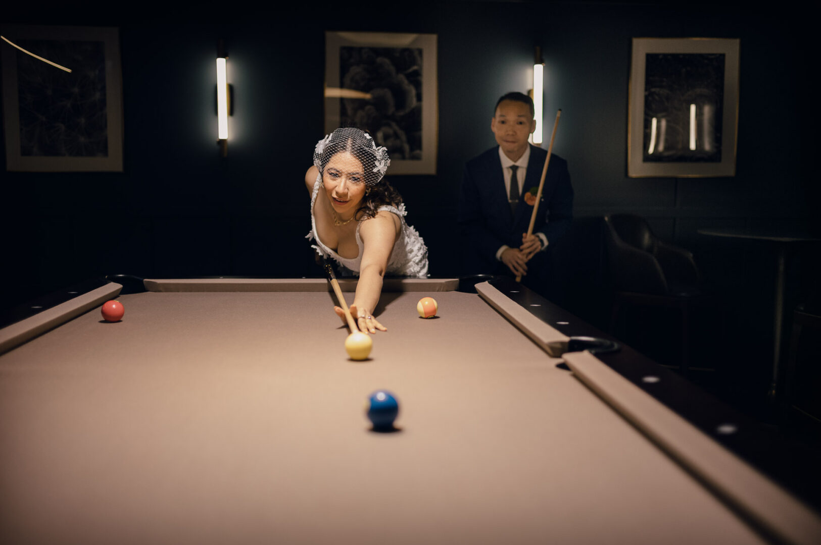 Bride playing pool with groom nearby.