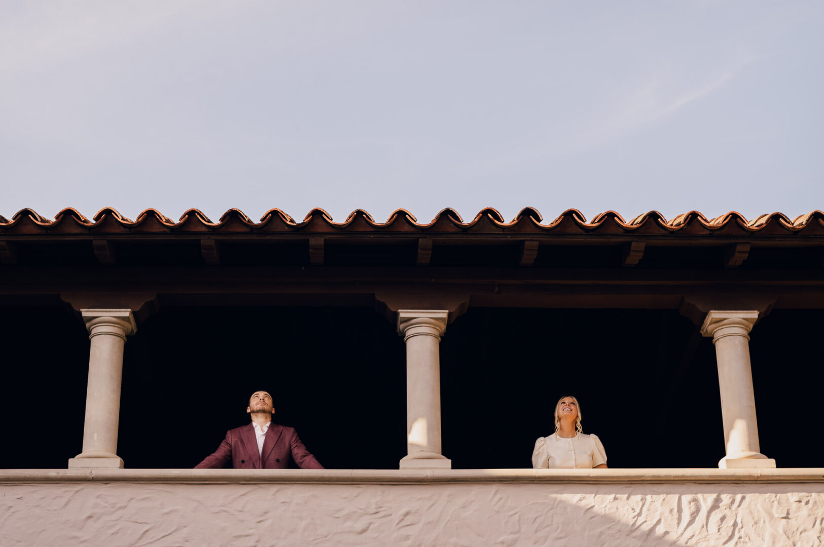 Couple standing on balcony, looking up.