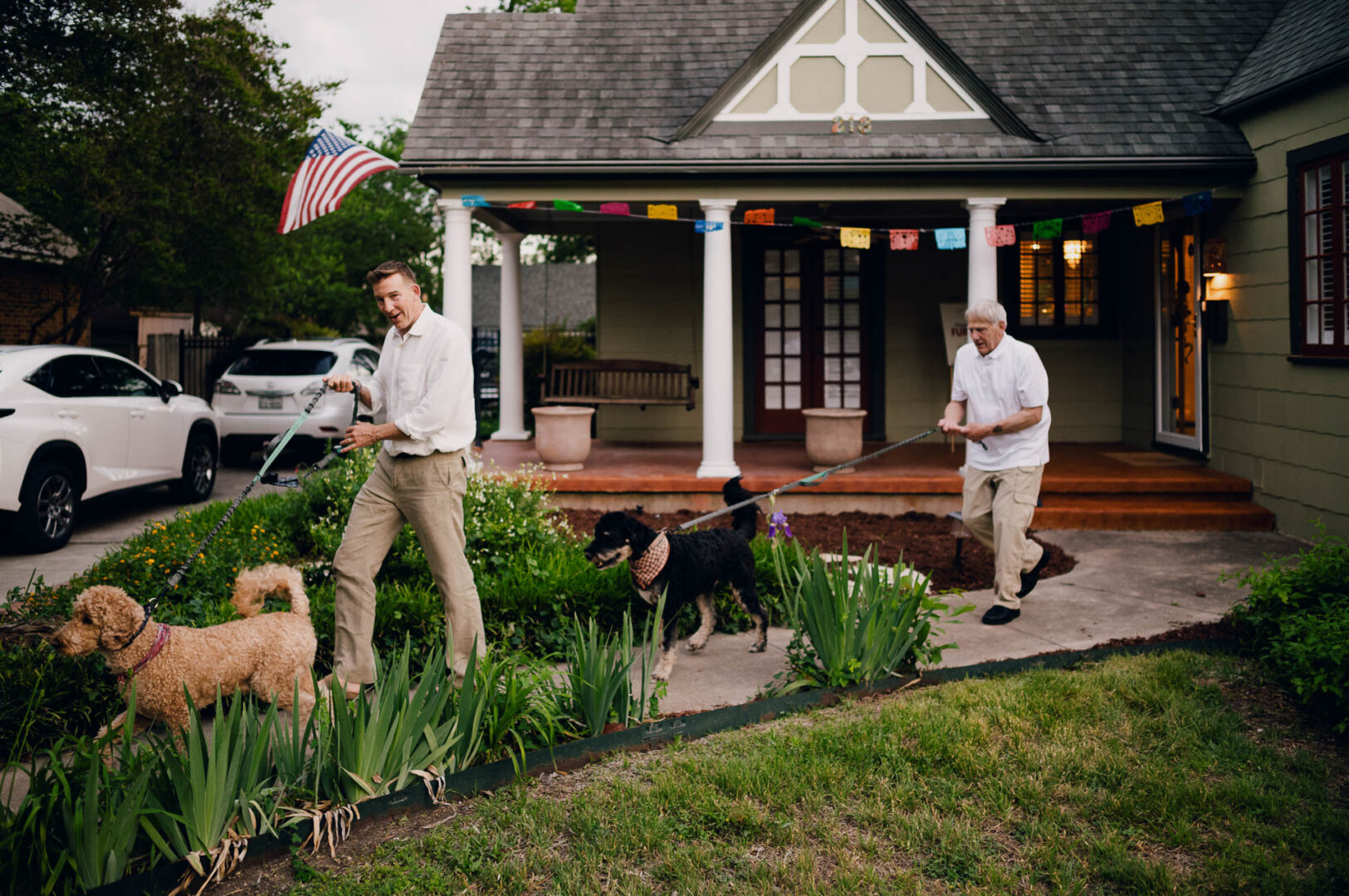 Candid backyard wedding scene with guests walking near a historic home and garden before the celebration.