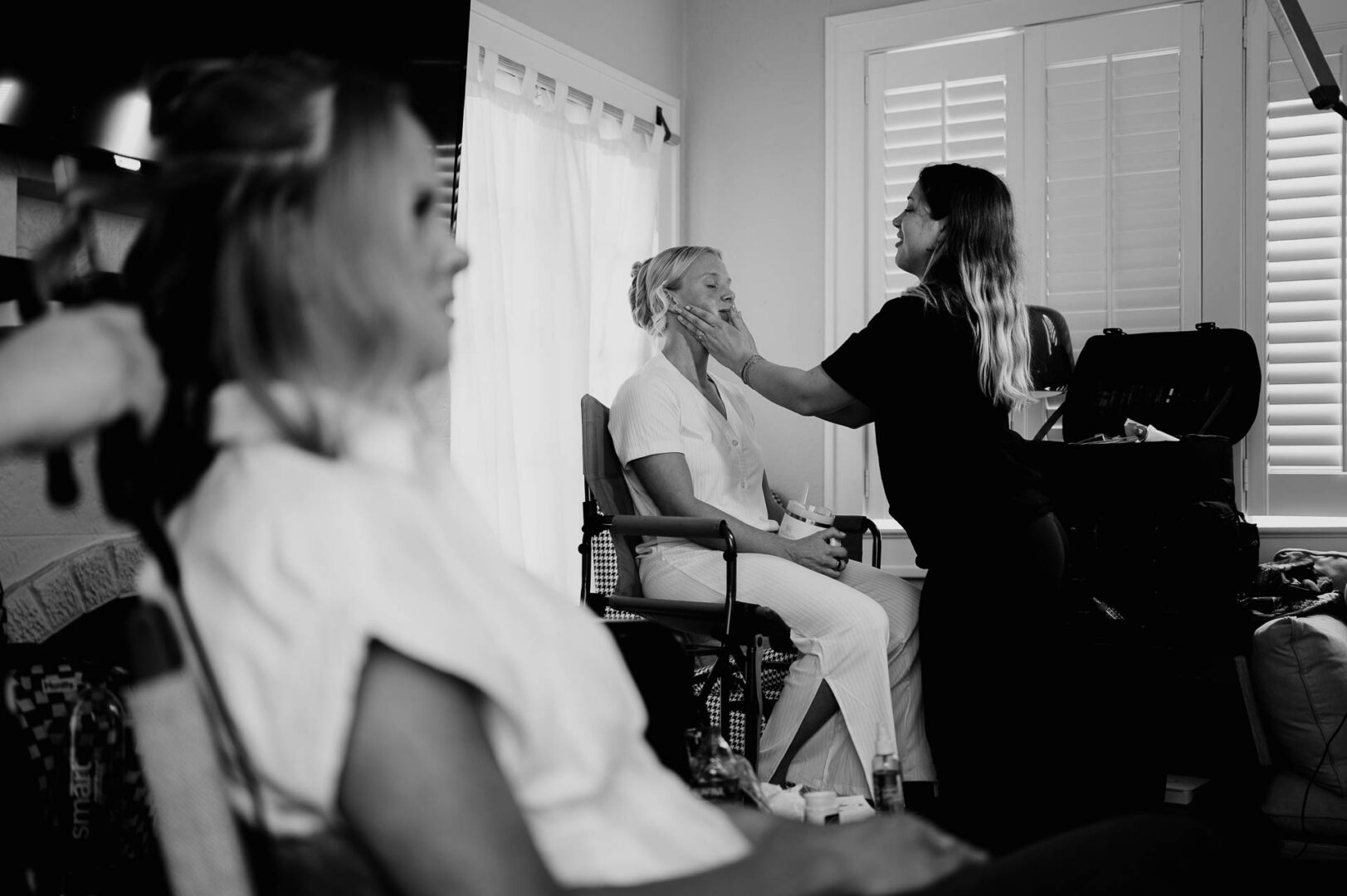 Black and white wedding preparation photo of makeup being applied indoors.