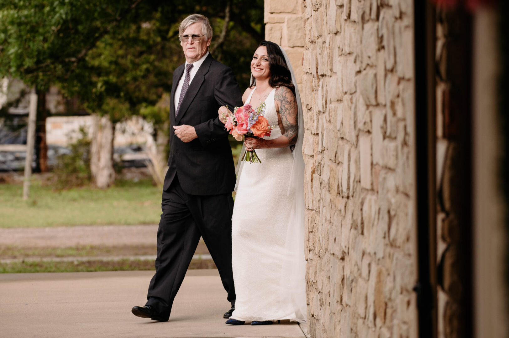 Vibrant Spring Wedding at Shiraz Gardens in Bastrop 22 Documentary wedding photo of the bride walking with her father at Shiraz Gardens in Bastrop, Texas.