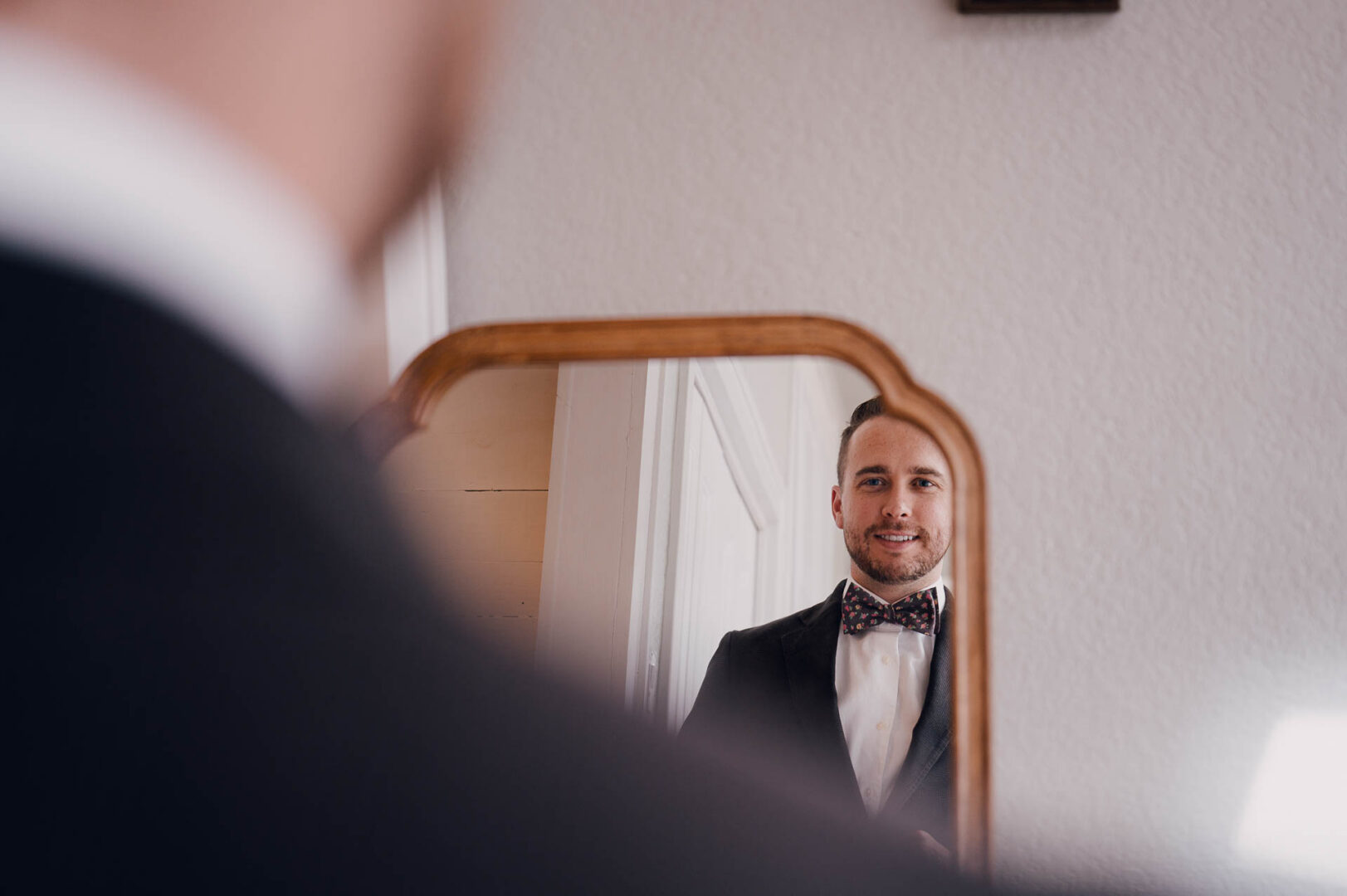 Groom reflected in a mirror while preparing for the wedding in a tuxedo.