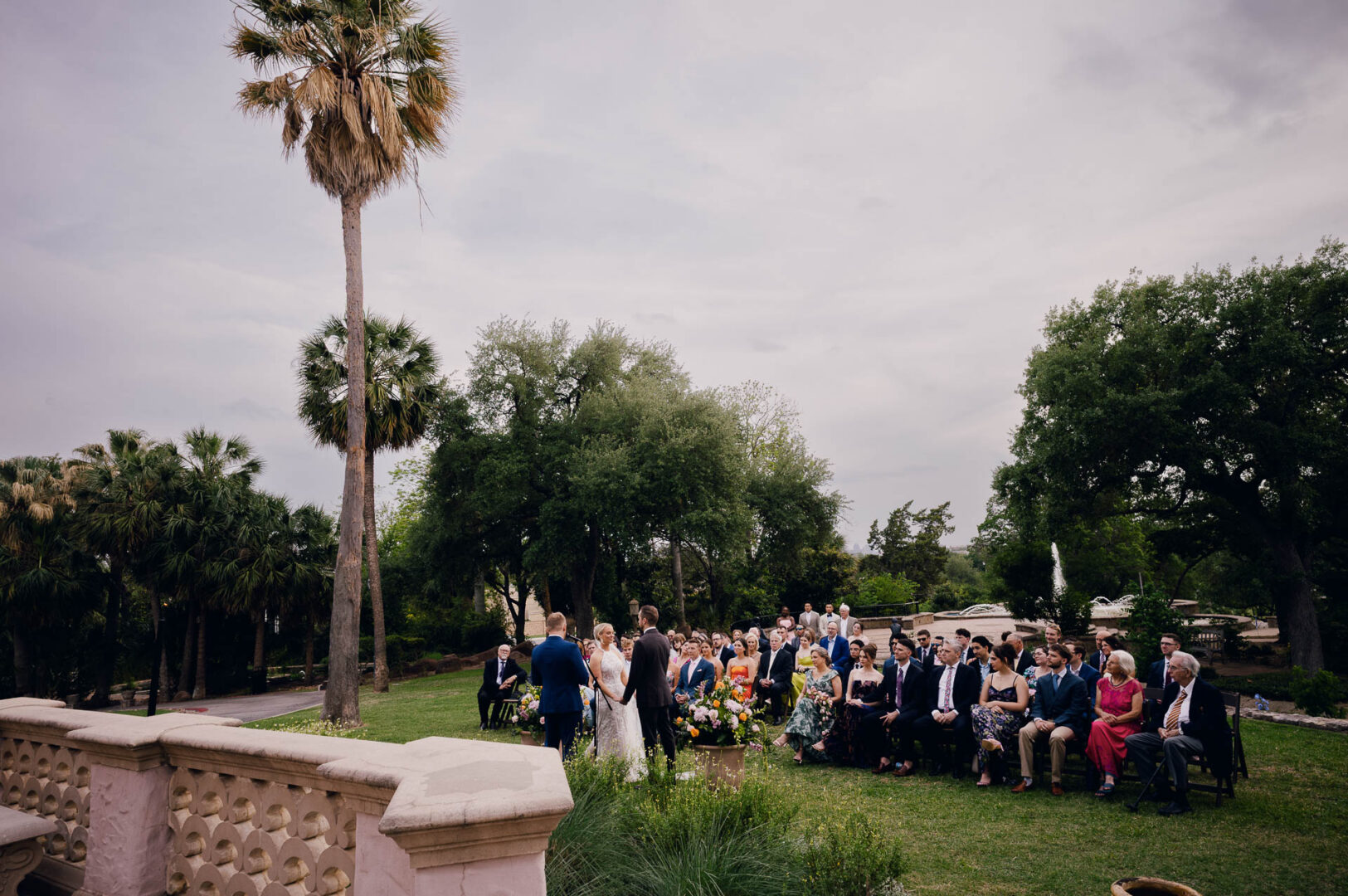 Outdoor wedding ceremony with guests seated in front of a historic venue.
