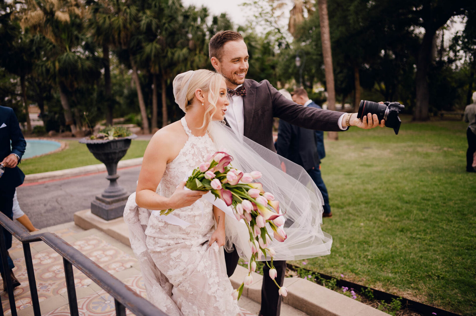 Bride and groom sharing a joyful outdoor moment with guests nearby.
