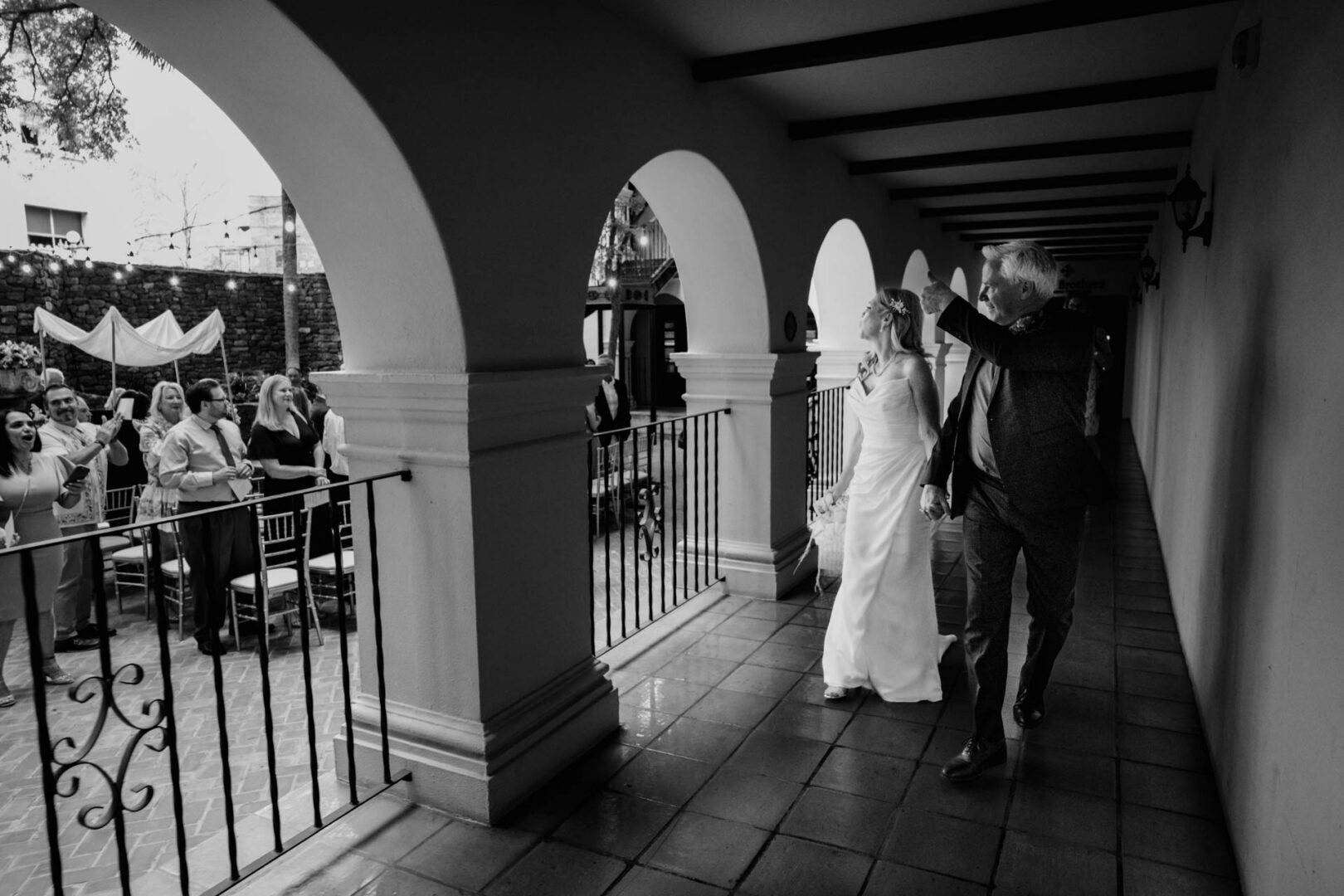 Black and white scene of couple and guests beneath arches at Omni La Mansión del Rio