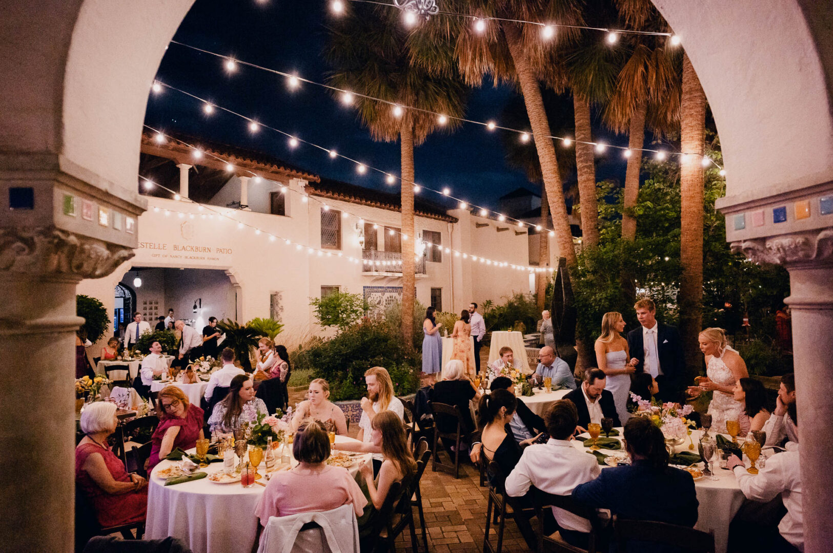 Guests seated at an outdoor wedding reception in a historic courtyard at night.