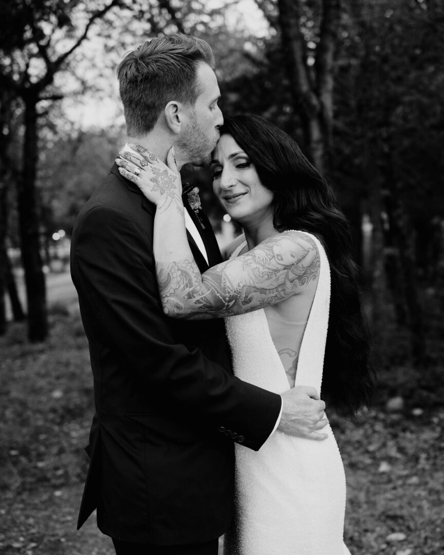 Vibrant Spring Wedding at Shiraz Gardens in Bastrop 55 Black and white wedding portrait of the bride and groom embracing among the trees at Shiraz Gardens in Bastrop, Texas.