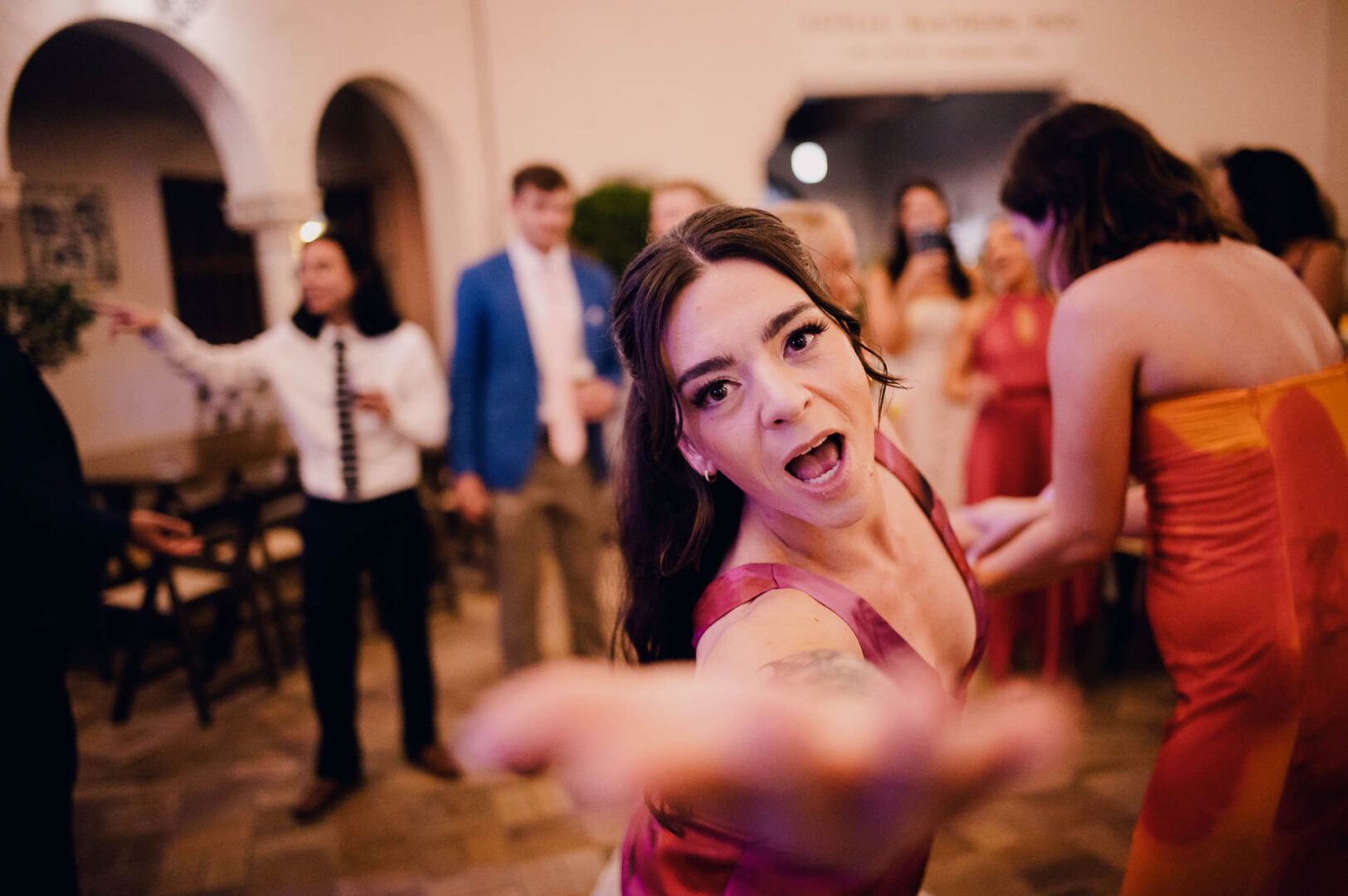 Bridesmaid pointing toward the camera during a lively wedding reception dance floor moment.