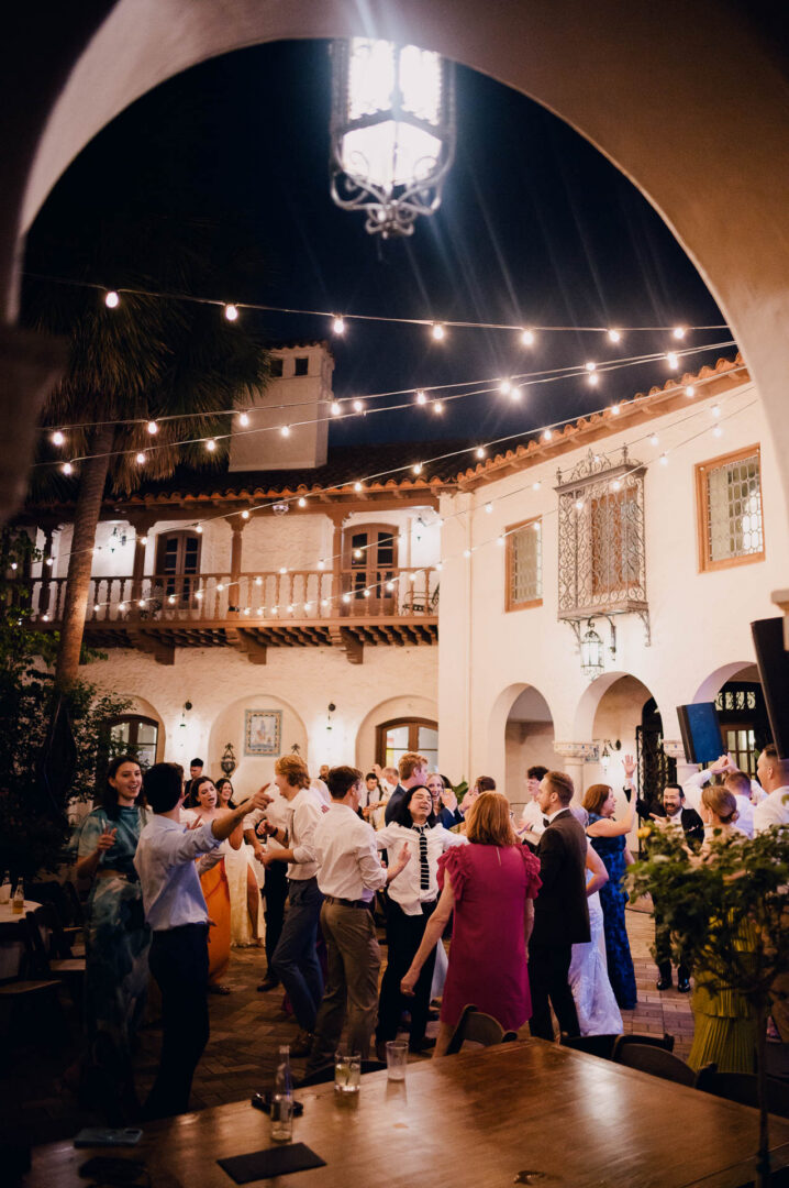 Evening wedding reception in a historic courtyard with guests seated under string lights.