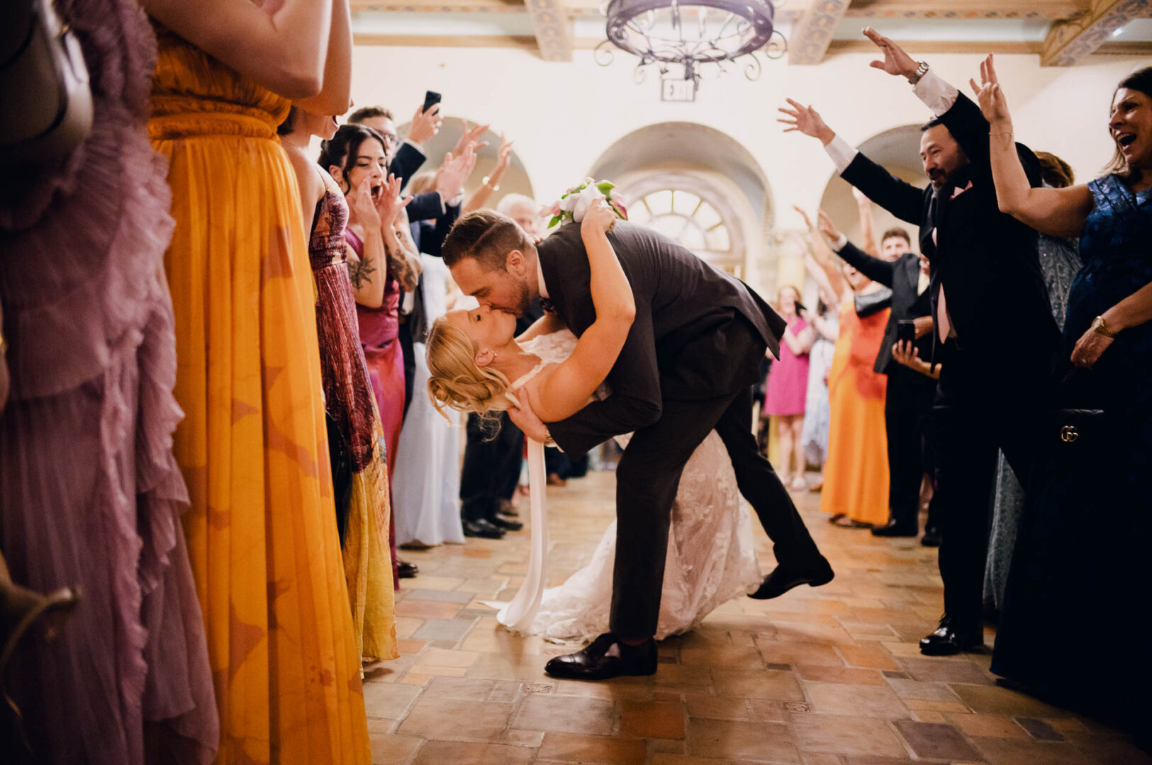 Bride and groom kissing under colorful streamers during their wedding exit.