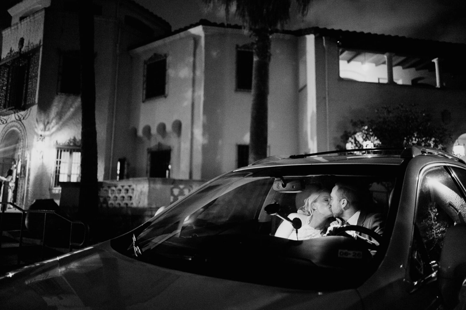 Black and white nighttime wedding photo of a vintage car parked outside a historic venue.