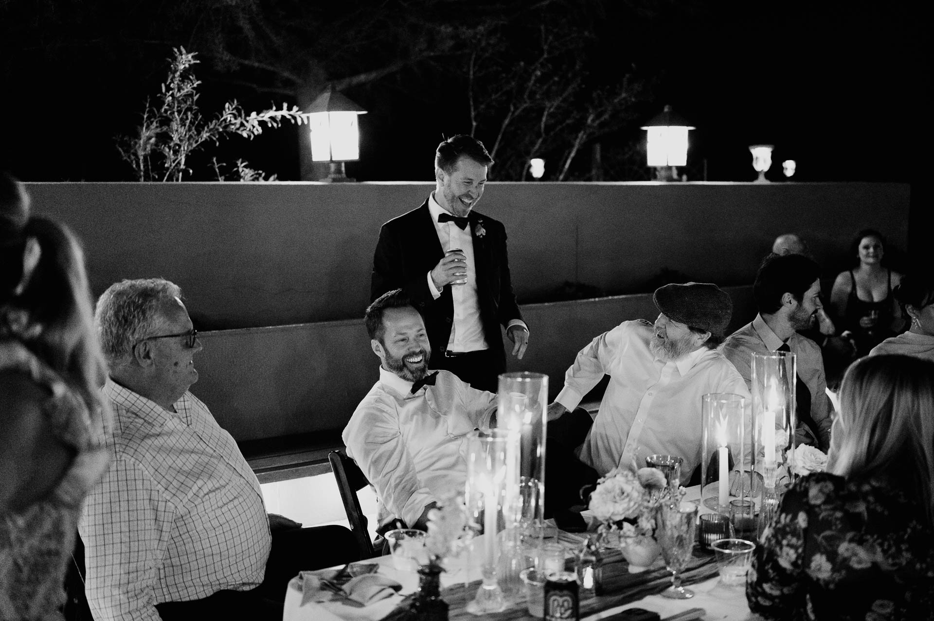 Documentary Wedding Portfolio | Philip Thomas 210 Black and white candid wedding reception photo of guests seated together at Shiraz Gardens in Bastrop, Texas.