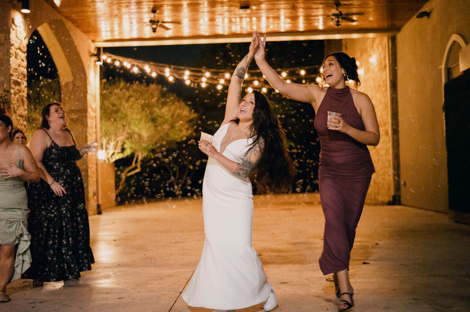 Vibrant Spring Wedding at Shiraz Gardens in Bastrop 86 Wedding reception photo of the bride dancing with a guest beneath the pavilion at Shiraz Gardens in Bastrop, Texas.