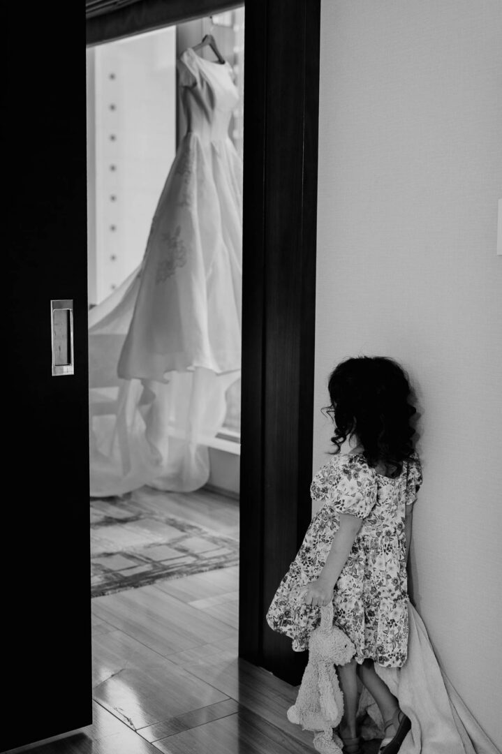 Black and white photograph of a wedding dress hanging in a doorway.