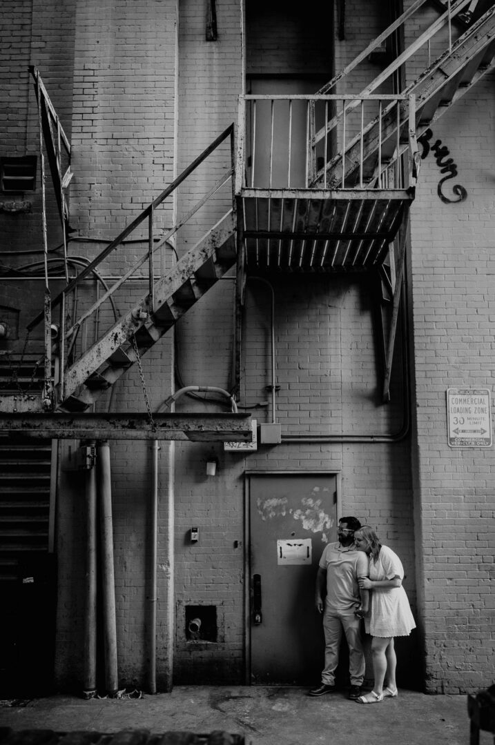 Couple embracing near industrial backdrop.