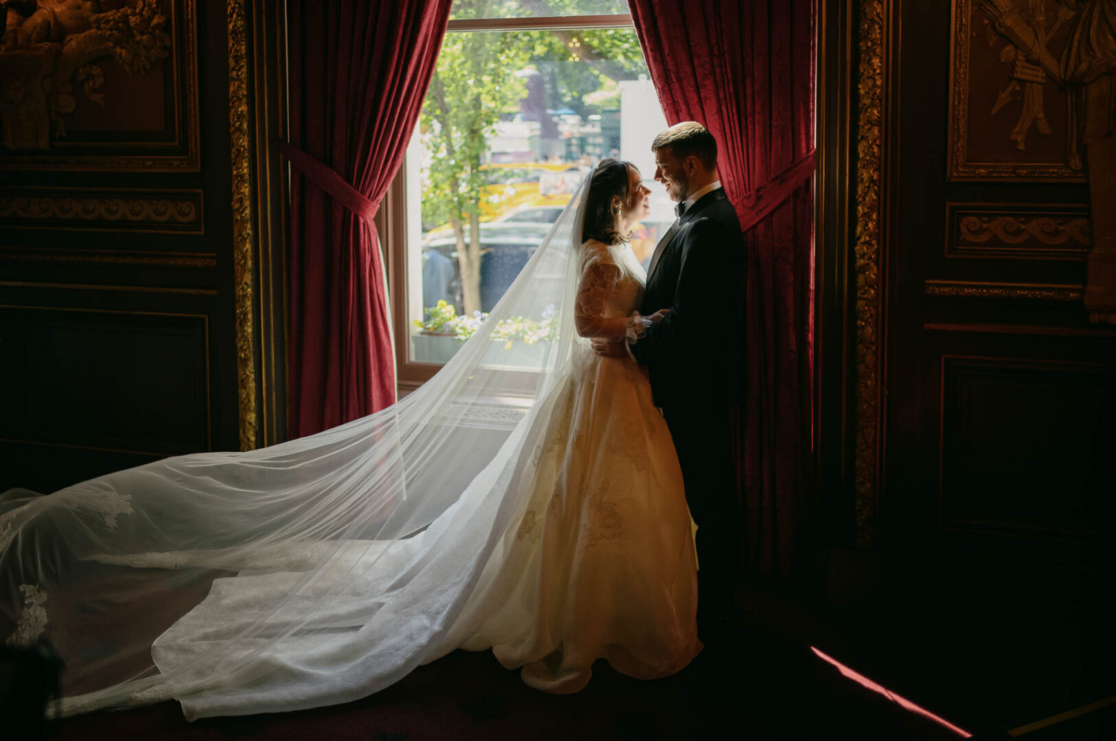 Bride and groom standing by red curtains at The Metropolitan Club.