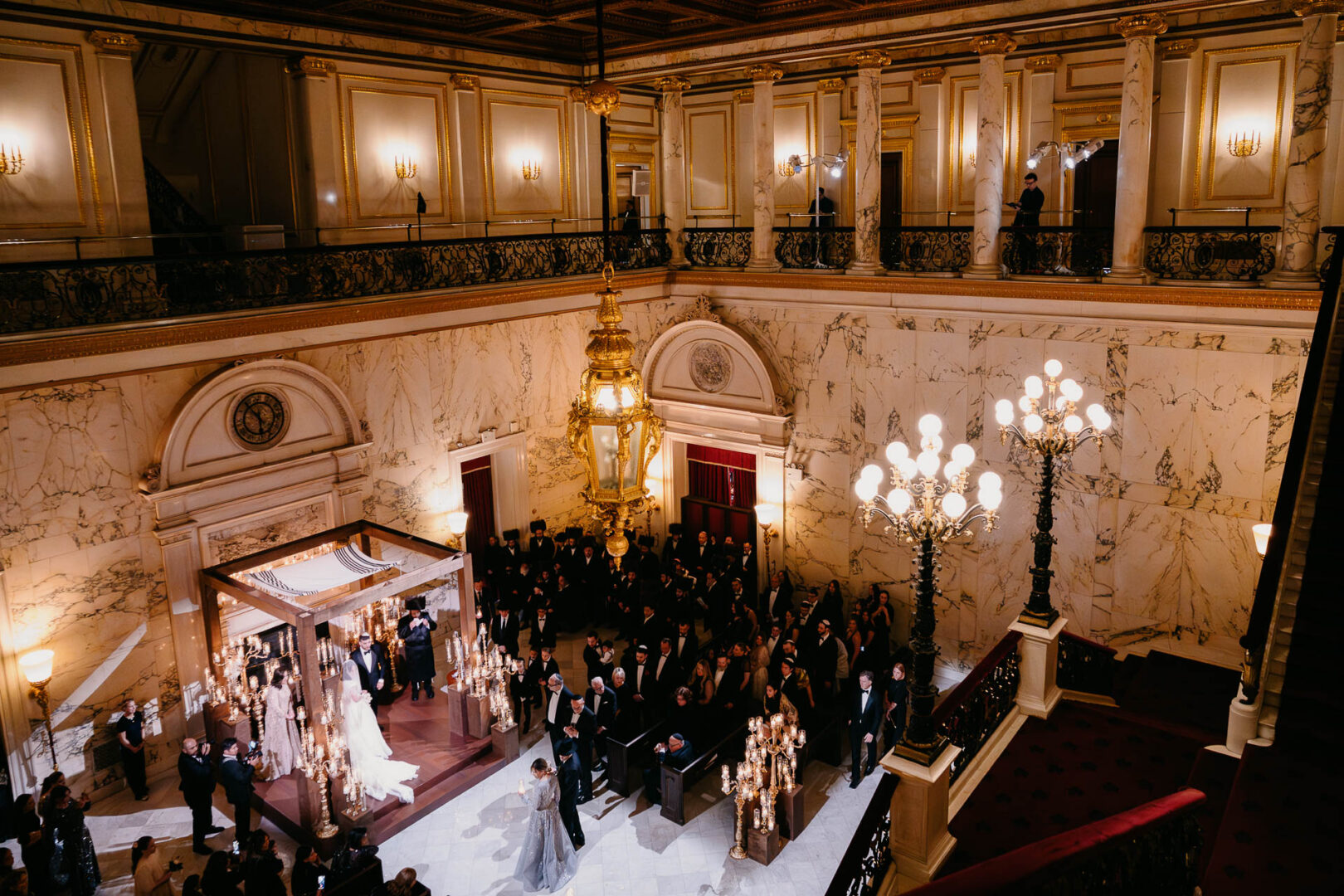 Wide view of the ceremony room with guests seated beneath chandeliers.