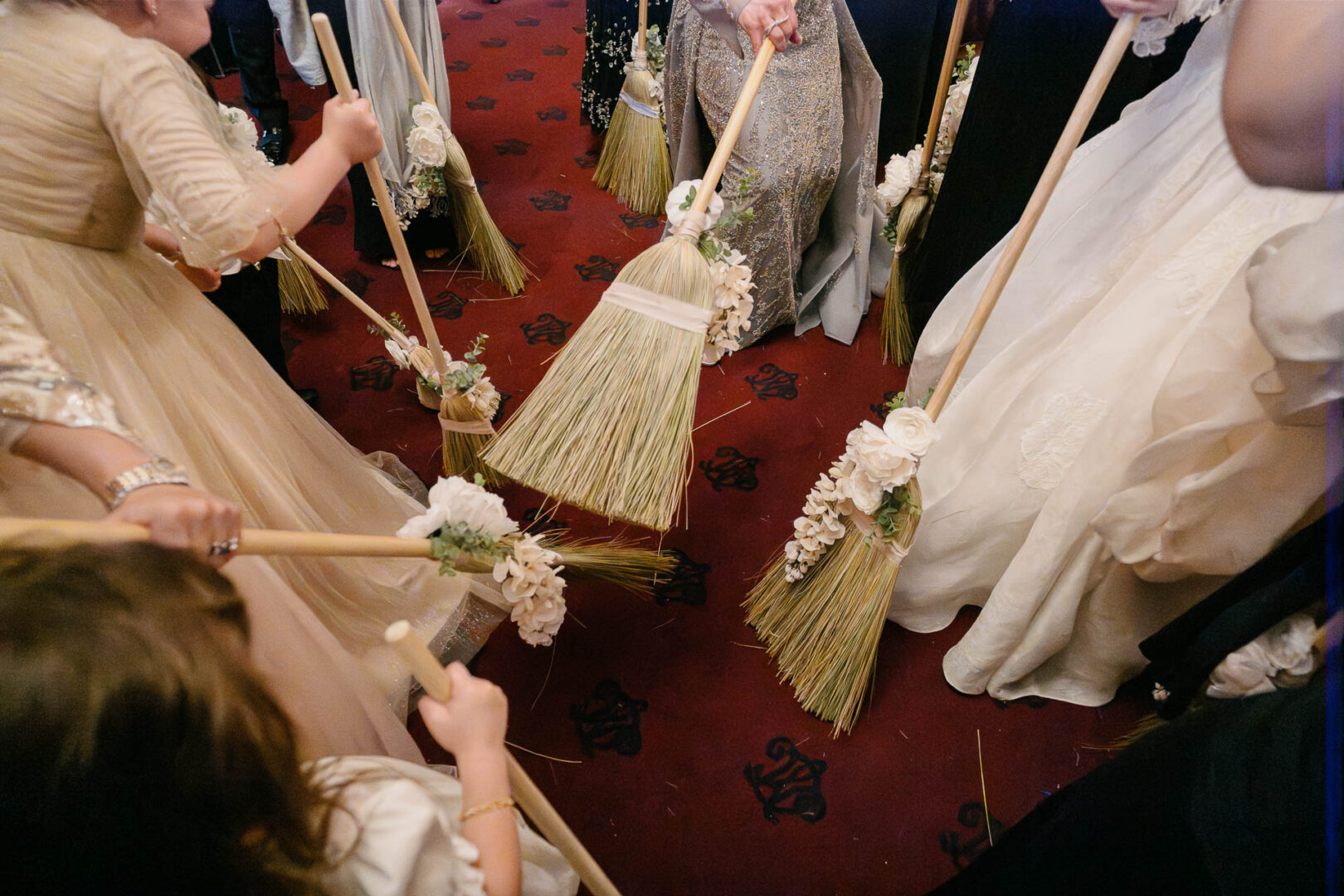 Guests holding decorated brooms at wedding.