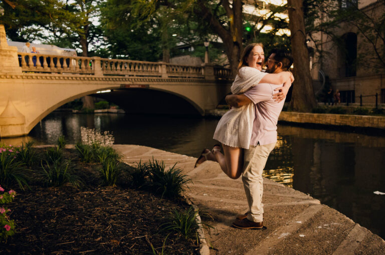 Couple joyfully embracing in a downtown engagement session by the riverwalk in San Antonio.