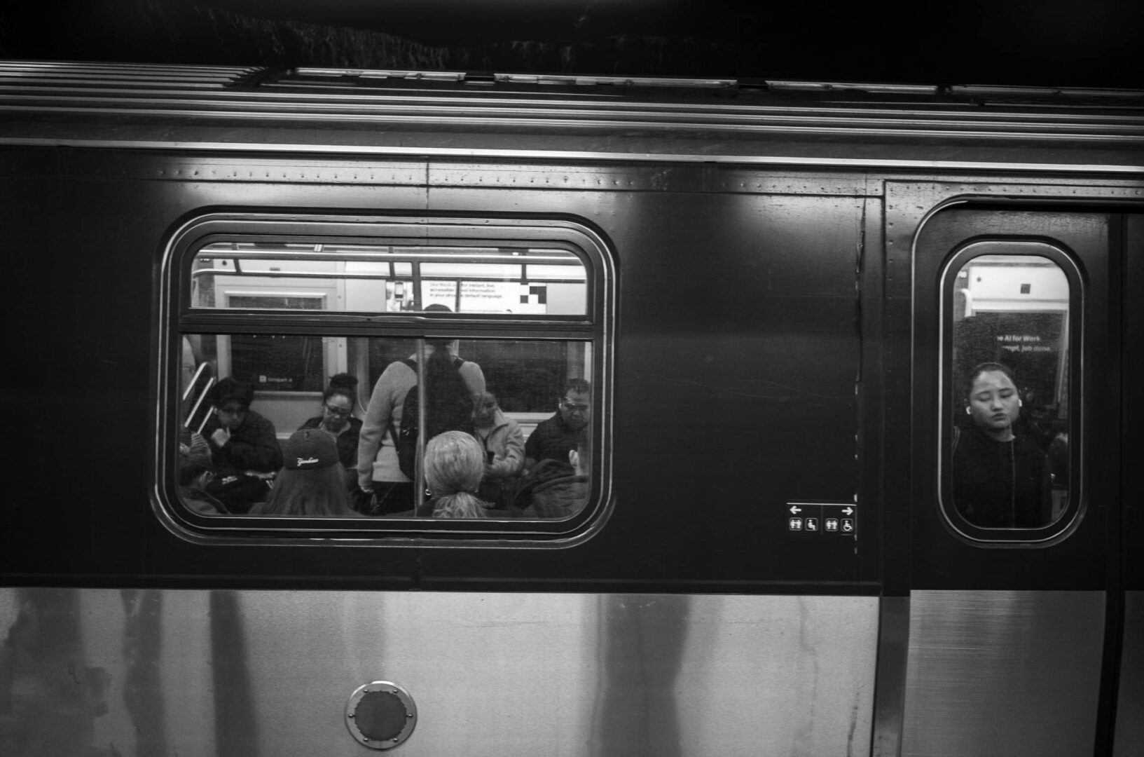 NYC in May: Street Photography in New York City 4 lack-and-white street photograph of subway passengers seen through the windows of a train stopped at a New York City station.