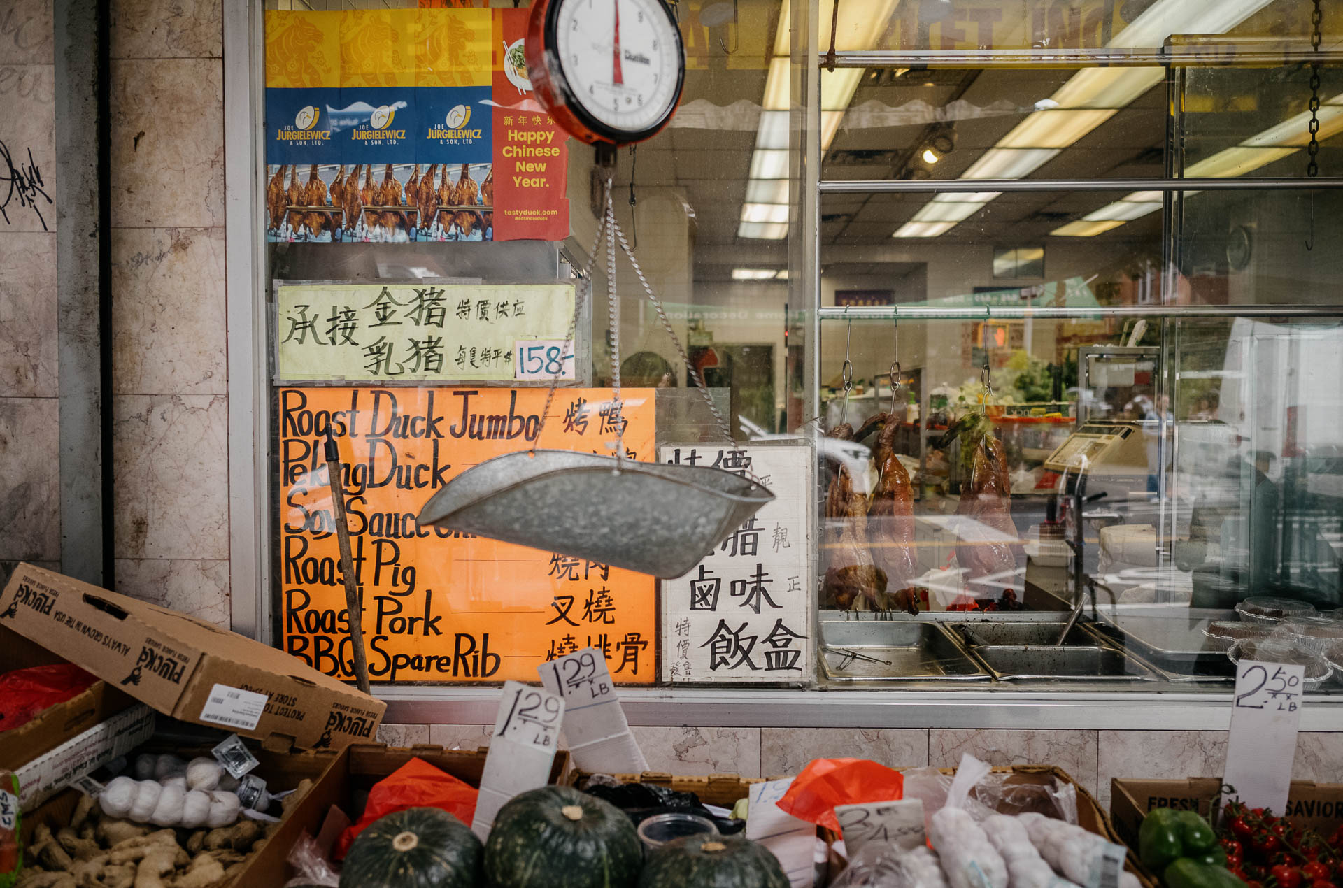 Street + urban photography 134 Color street photograph of a Chinatown market window displaying roast duck, handwritten signs, produce, and a hanging scale in New York City.