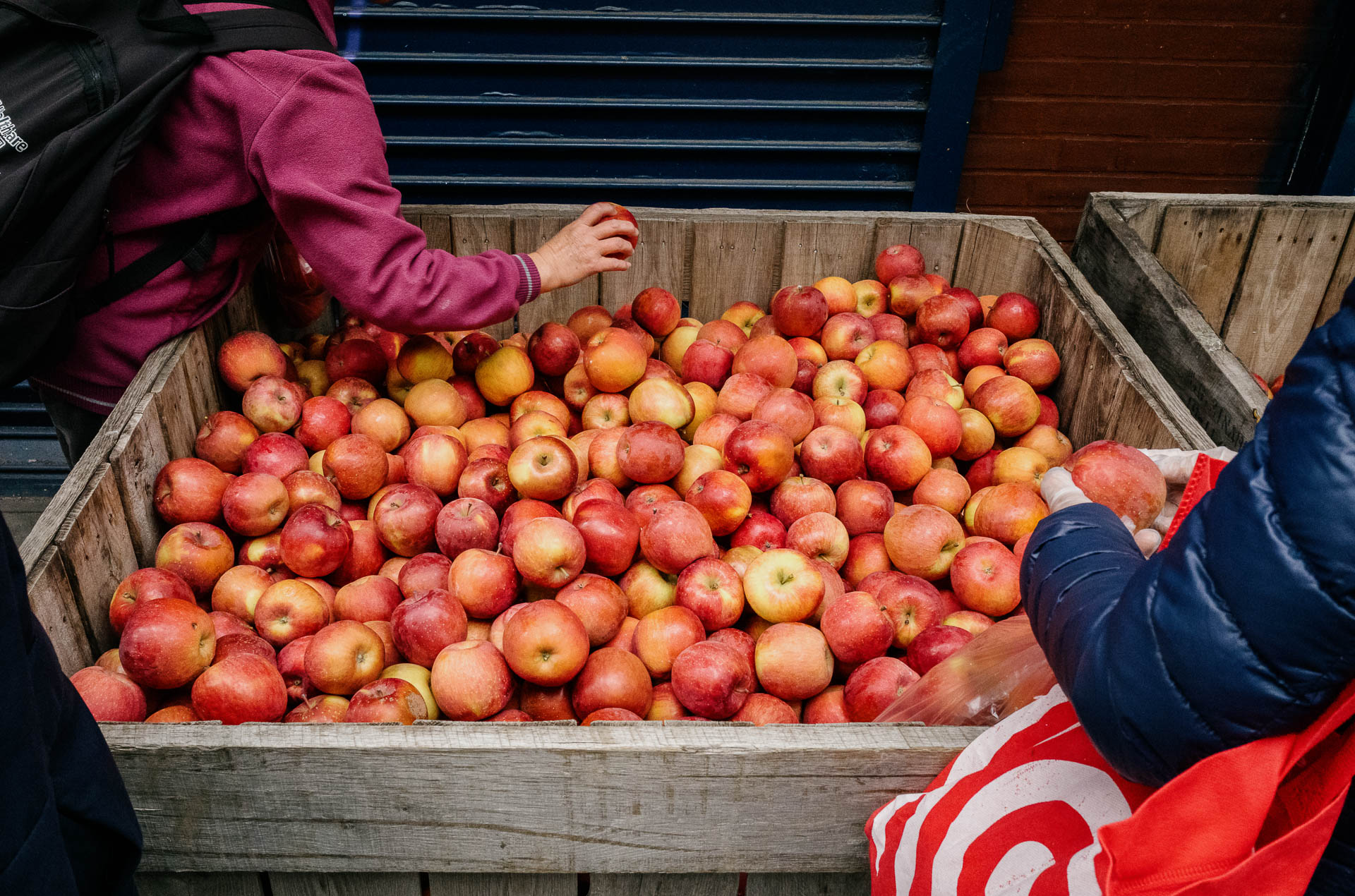 Street + urban photography 135 Color street photograph of two shoppers selecting apples from a large wooden produce bin outside a Chinatown market in New York City.