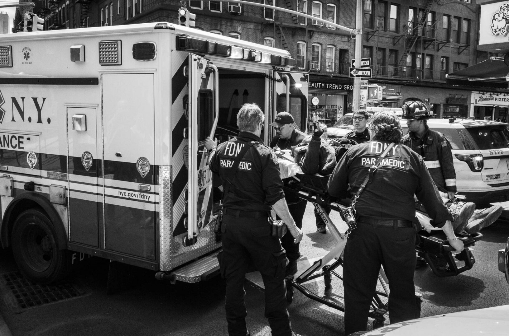 NYC in May: Street Photography in New York City 11 Black-and-white documentary photograph of FDNY paramedics moving a patient on a stretcher into an ambulance on a New York City street.