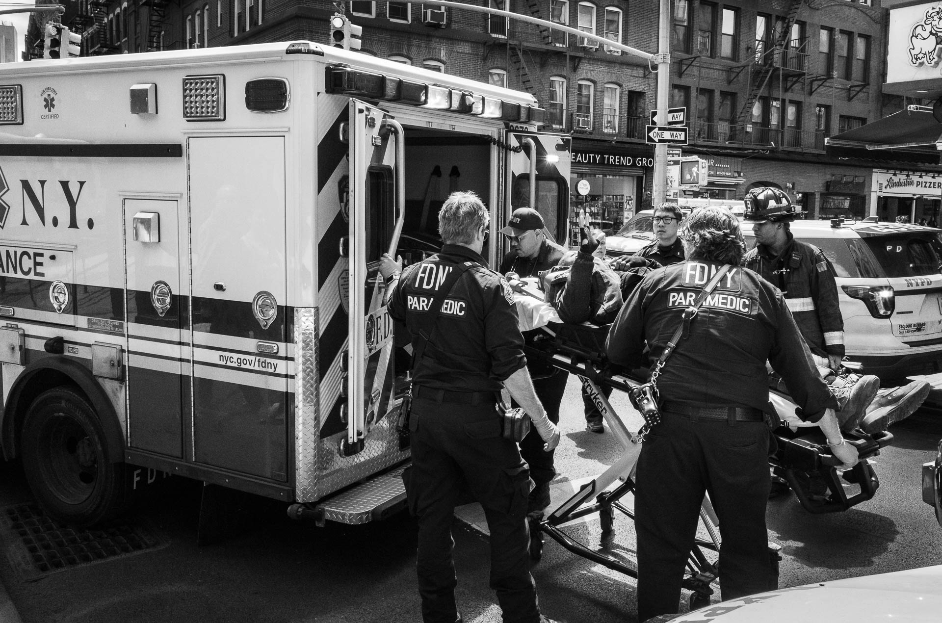 Street + urban photography 140 Black-and-white documentary photograph of FDNY paramedics moving a patient on a stretcher into an ambulance on a New York City street.