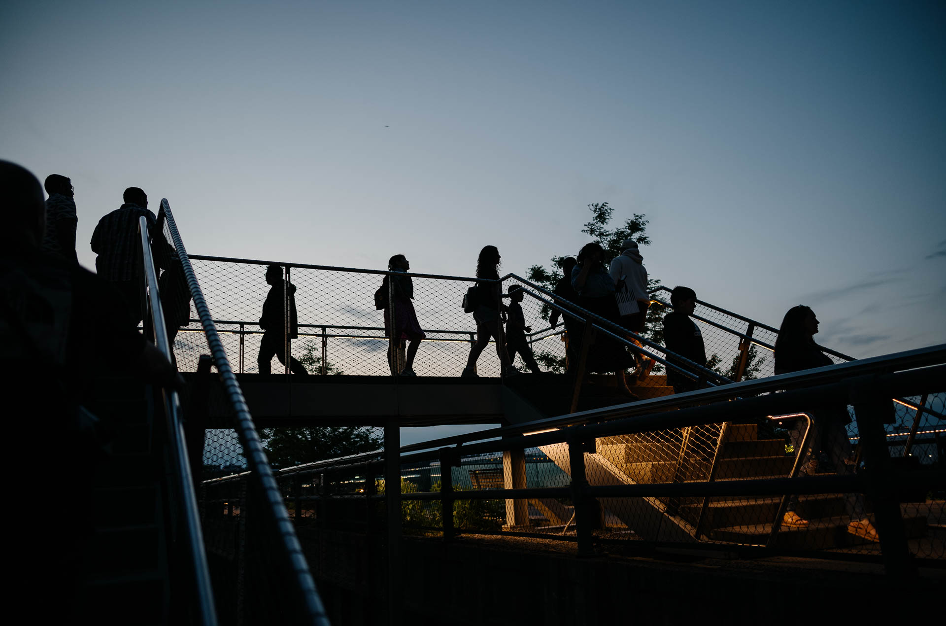 Street + urban photography 150 Color photograph of pedestrians silhouetted against the evening sky as they move along an elevated walkway in New York City.