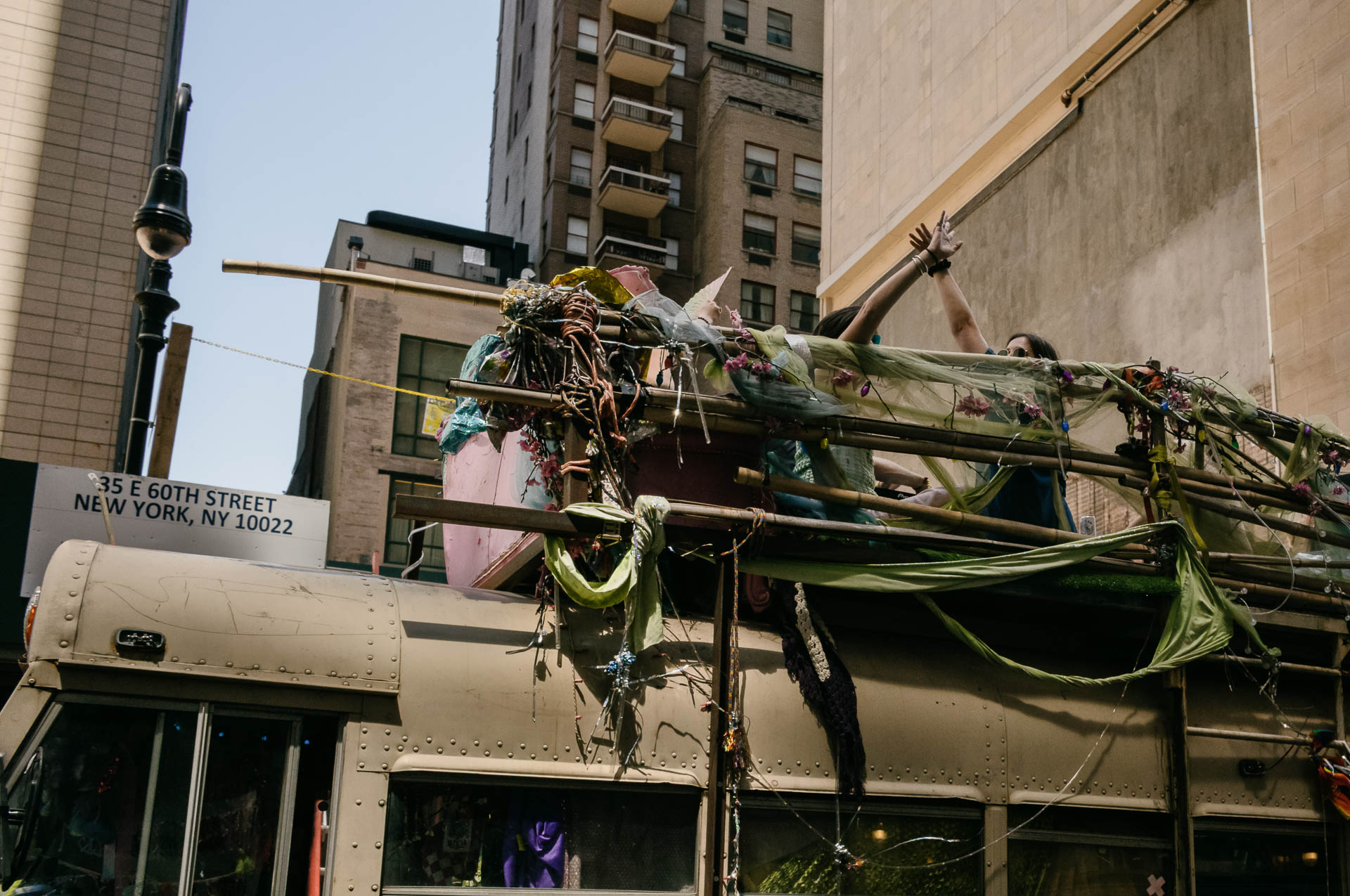 Street + urban photography 152 Color street photograph of a person raising both arms from the upper level of a decorated vehicle on East 60th Street in Manhattan.