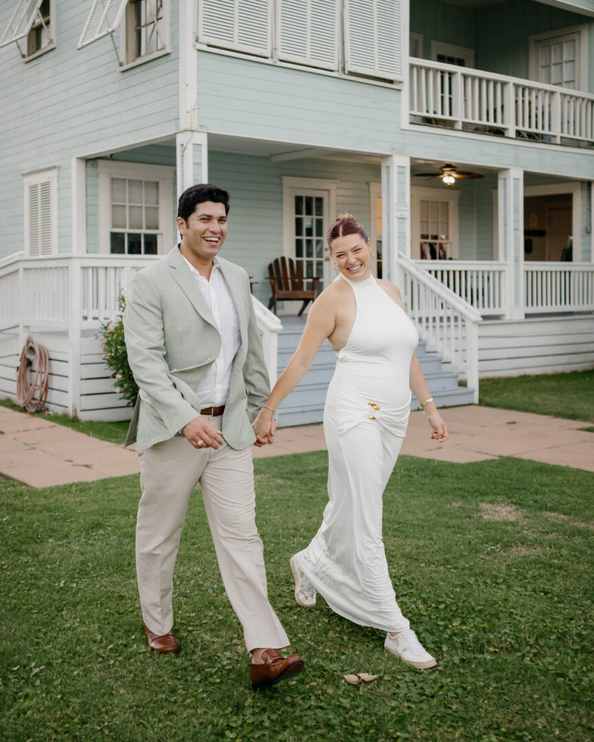 Chapel on the Dunes Wedding | Port Aransas, Texas | Mady+Roland 7 The couple walks hand-in-hand along the porch of a coastal cottage-style building at Roosevelt's, she in a white dress, he in a light suit.