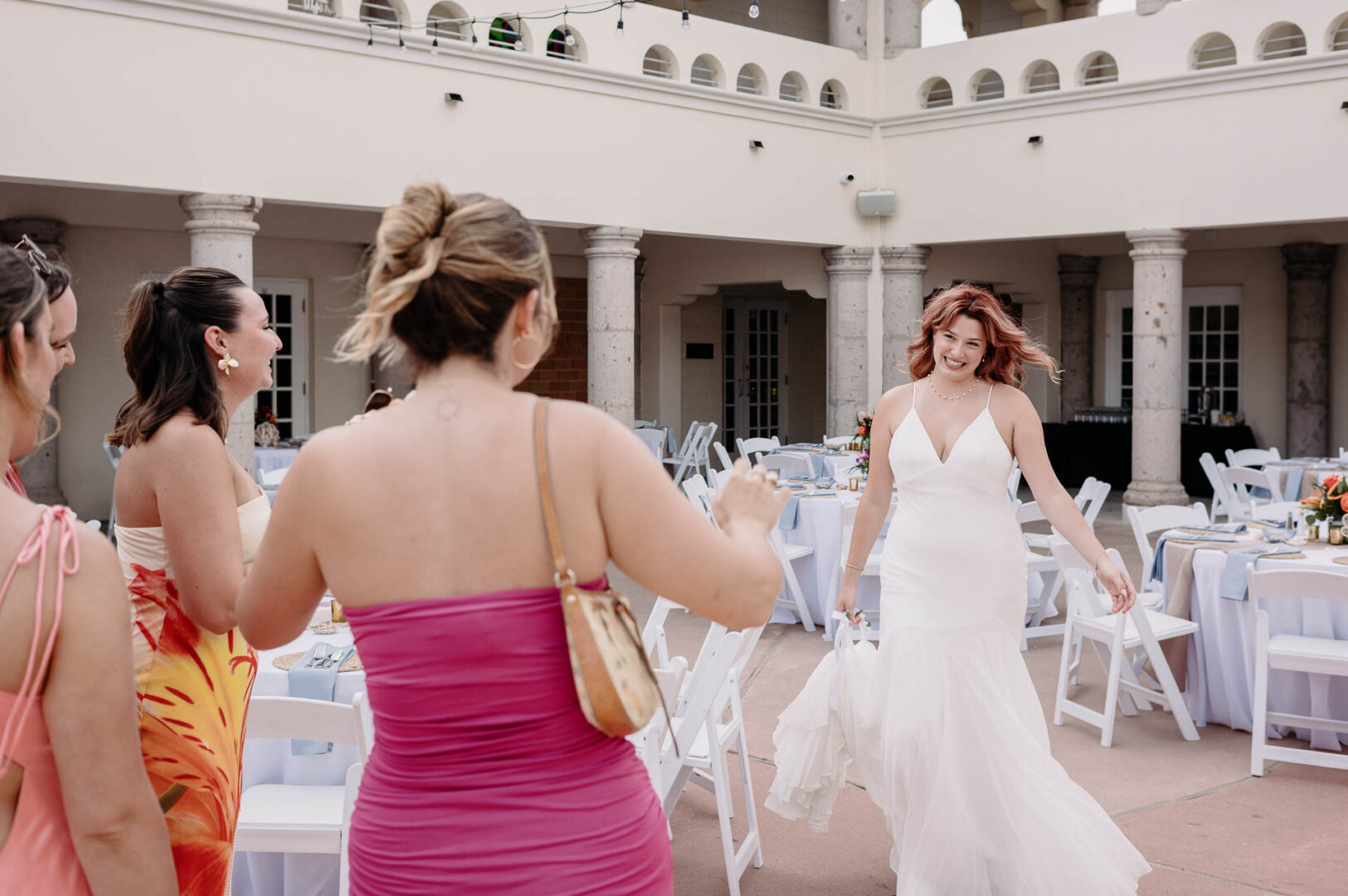 Chapel on the Dunes Wedding | Port Aransas, Texas | Mady+Roland 39 Two women in dresses walk together across an open courtyard toward reception tables.