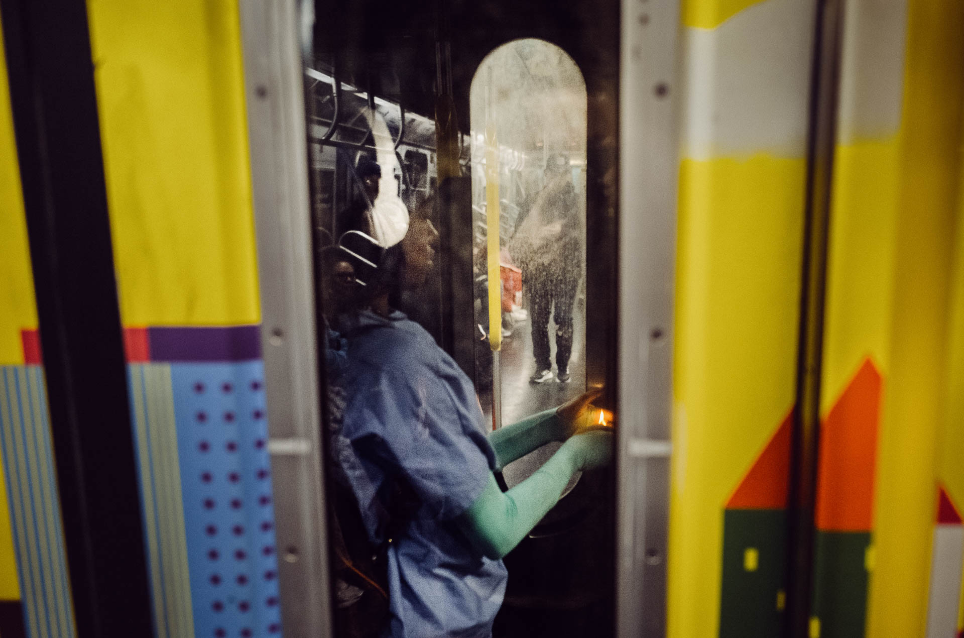 Street + urban photography 8 A passenger straddles the space between two subway carriages, smoking as the train moves through the city. Framed through the narrow doorway, the figure is surrounded by bold color, reflections, and the worn surfaces of the train—an uneasy, fleeting moment hidden between cars.