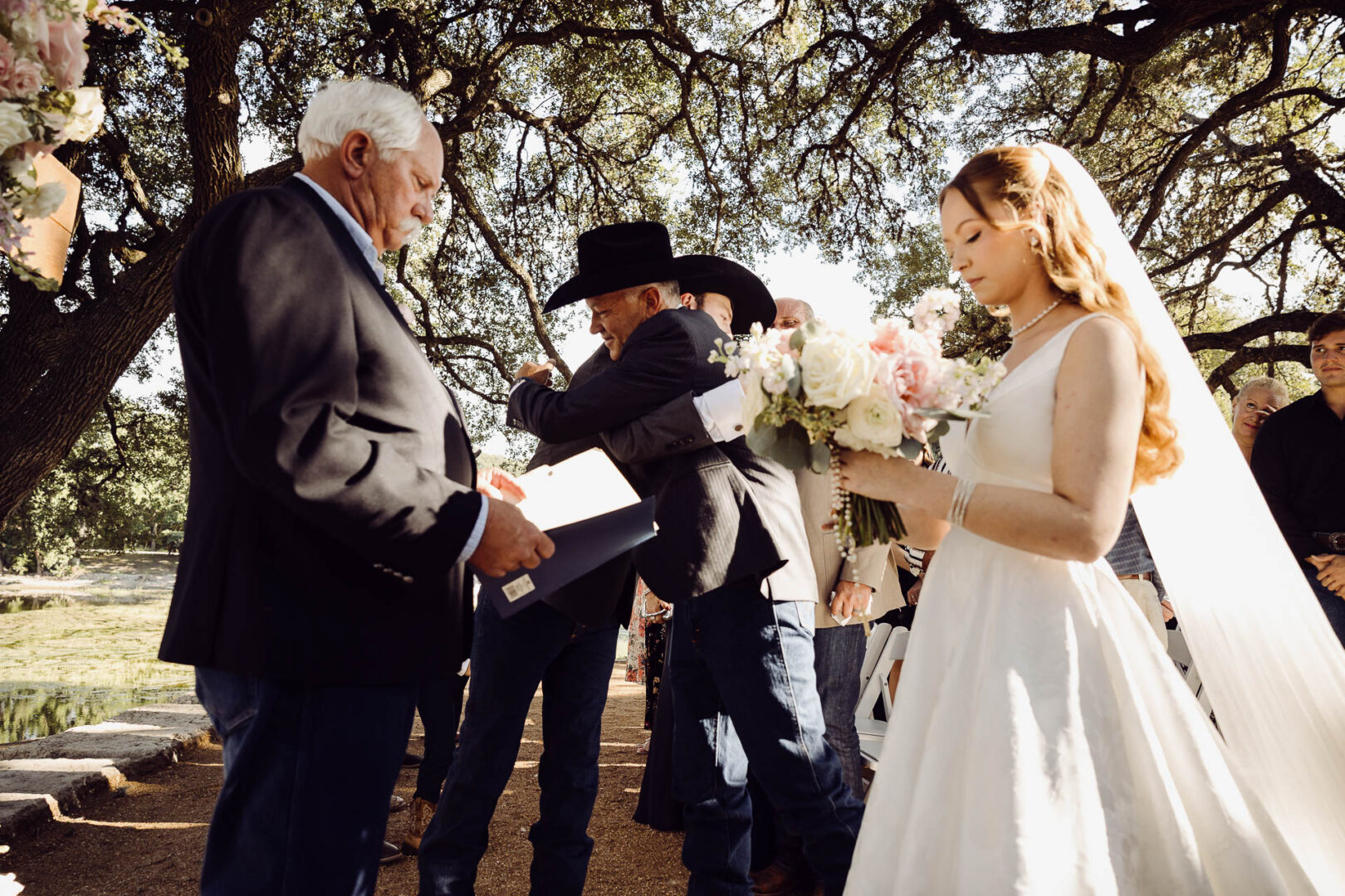 Tapatio Springs Hill Country Resort | Luana + Mack | Helotes 22 Father hugs the groom at the altar while the officiant reads from his folder, and the bride stands with her eyes closed in the foreground.